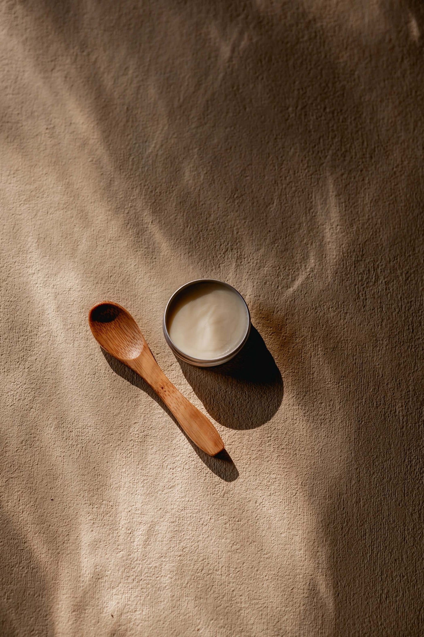 warm sfeerbeeld van een bovenaanzicht van een blik shea boter met een houten lepel ernaast