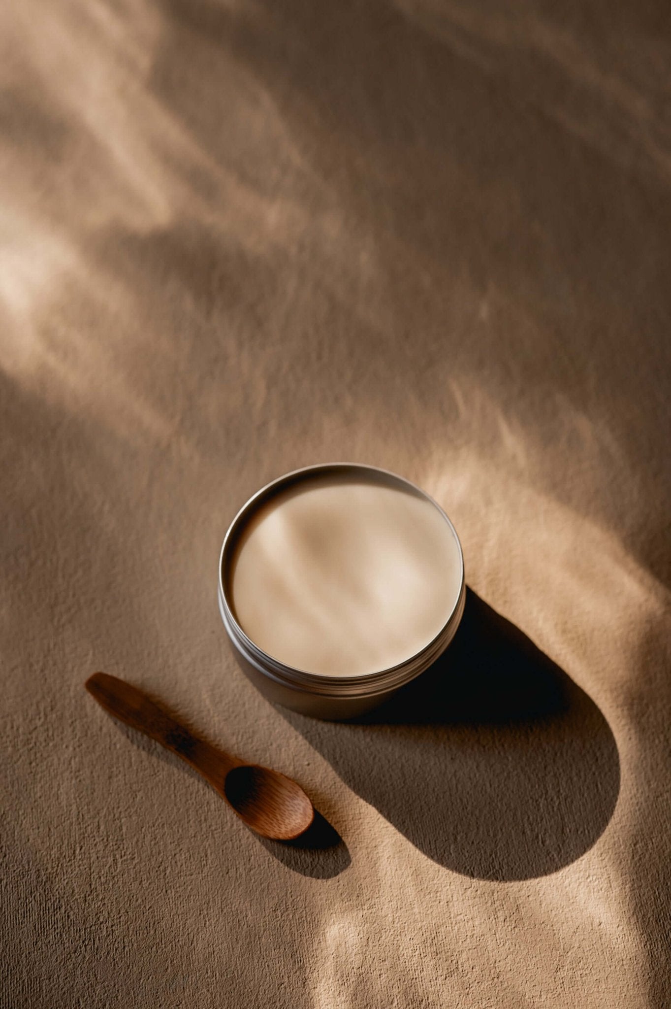 Namashea shea boter Kamille, open blik met houten lepeltje op een beige achtergrond, sfeervolle productfoto.