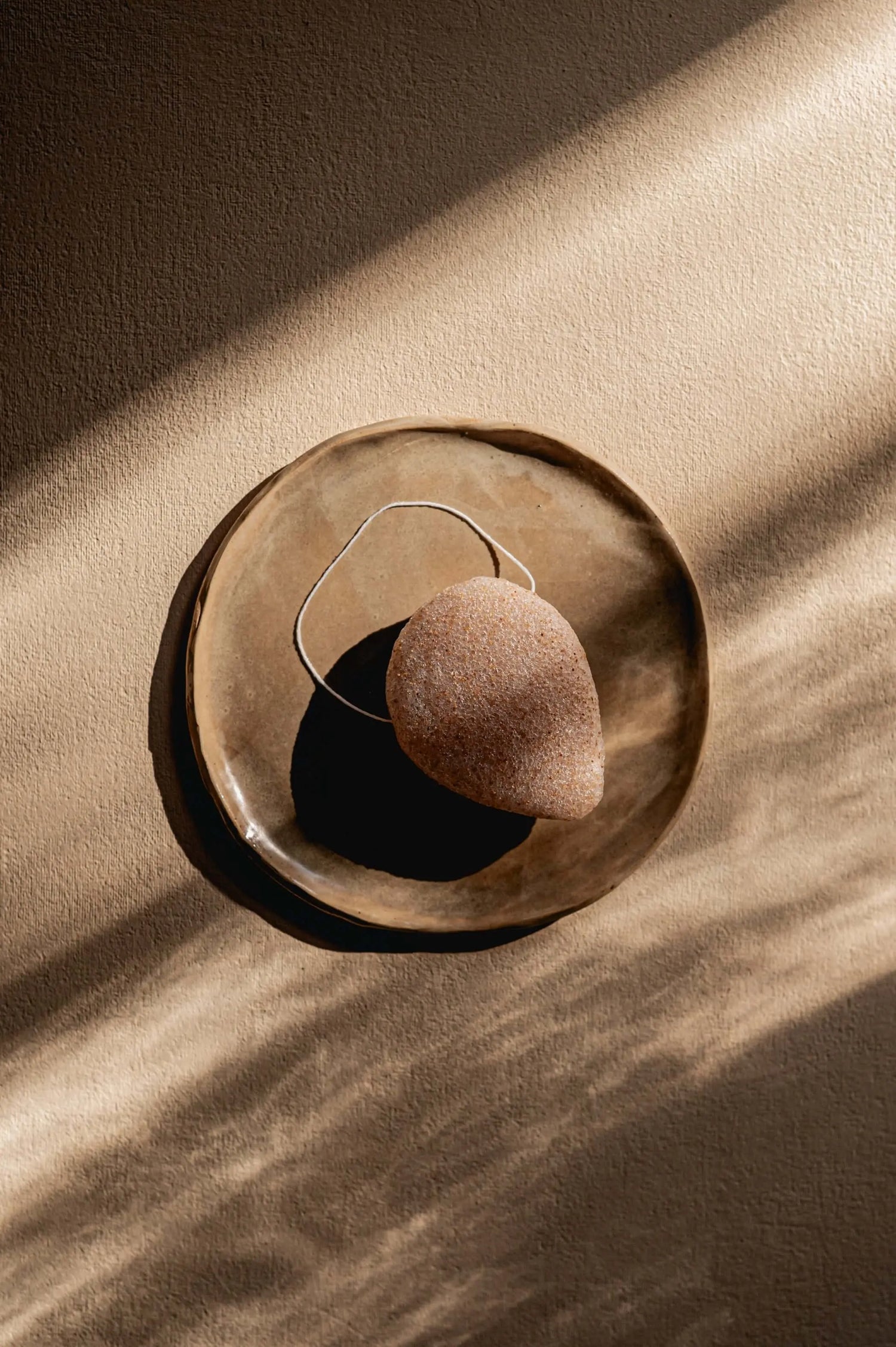 wit konjac sponsje ligt op houten schaaltje op wit tafelblad 