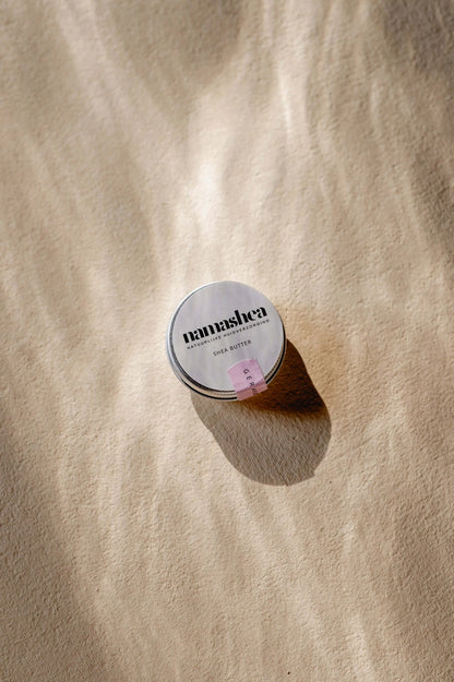 Shea butter tin canister on a sandy background, highlighting the natural skincare product with a minimalist design.