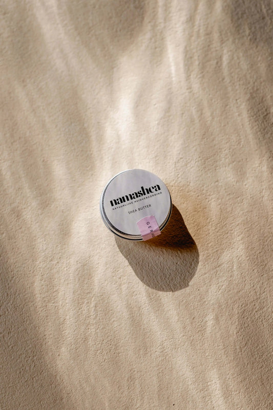 Shea butter tin canister on a sandy background, highlighting the natural skincare product with a minimalist design.