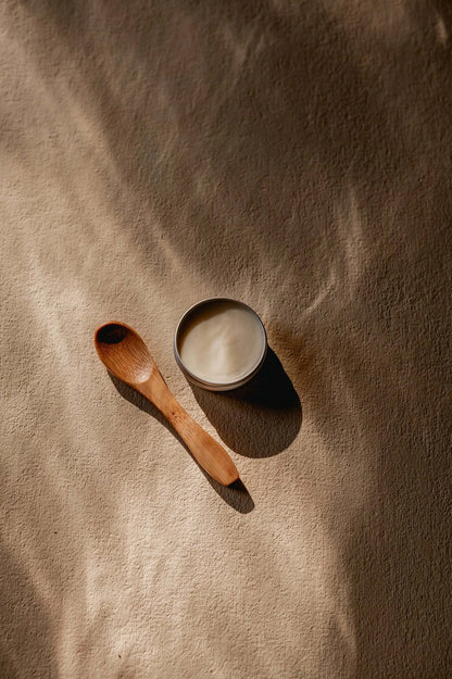 warm sfeerbeeld van een bovenaanzicht van een blik shea boter met een houten lepel ernaast