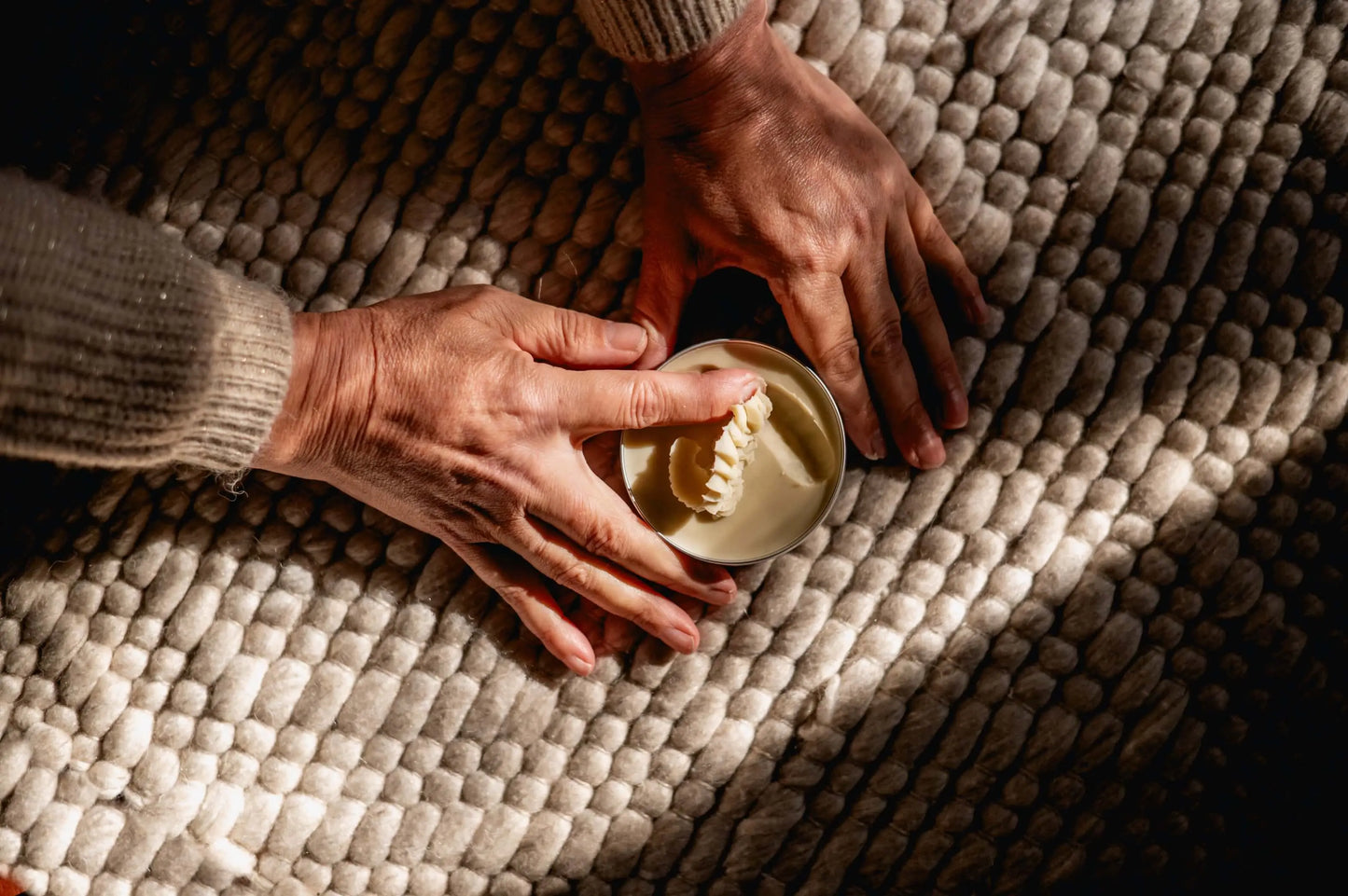 warm sfeerbeeld van handen die met een houten lepeltje door een blik shea boter roert