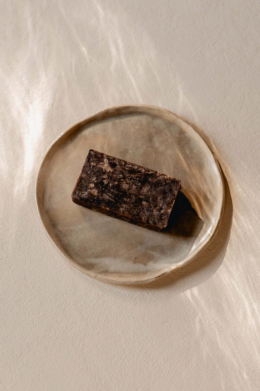 bovenaanzicht van een blok arican black soap van Namashea op een beige bord op een beige achtergrond