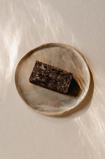 bovenaanzicht van een blok arican black soap van Namashea op een beige bord op een beige achtergrond