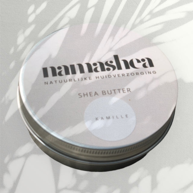 dicht blik shea boter van Namahsea met 100% zuivere kamille olie in de schaduw van een palmblad op grijze achtergrond 