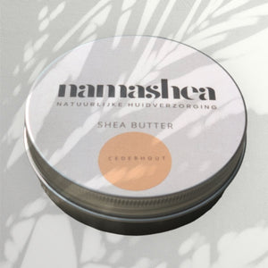 blik shea boter van Namashea met cederhoutolie op grijze achtergrond met palmbladschaduw