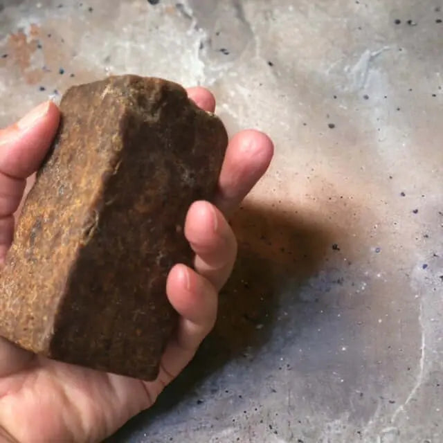 close up van een hand die boven een betonnen aanrecht een black zwarte zeep van Namashea vasthoudt